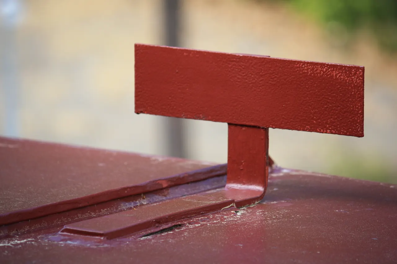 Arrêt de neige métallique rouge fixé sur une couverture de même teinte