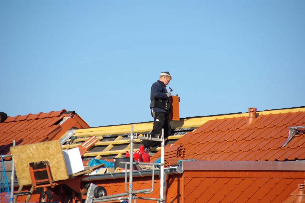 Couvreur au travail sur une toiture en tuiles orange en cours de pose, avec échafaudage