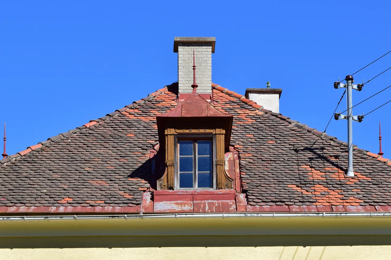 Lucarne à deux pans ouverte dans une couverture en tuiles, sous un ciel bleu